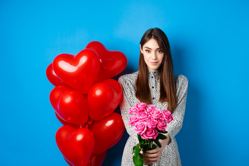 a woman holding a bouquet of roses and a bunch of red balloons