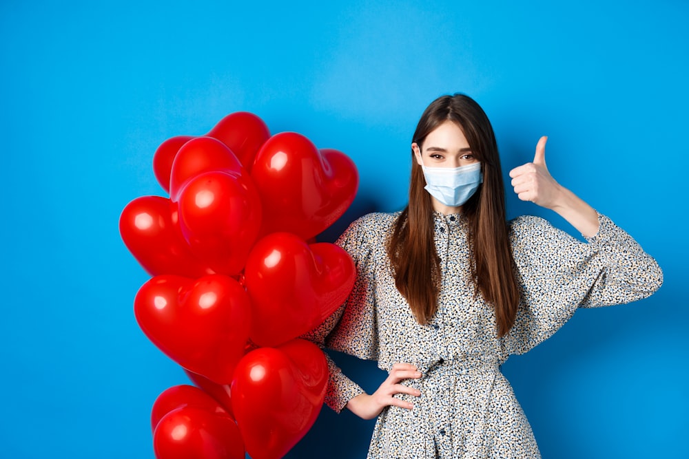 a woman wearing a face mask holding a bunch of red balloons