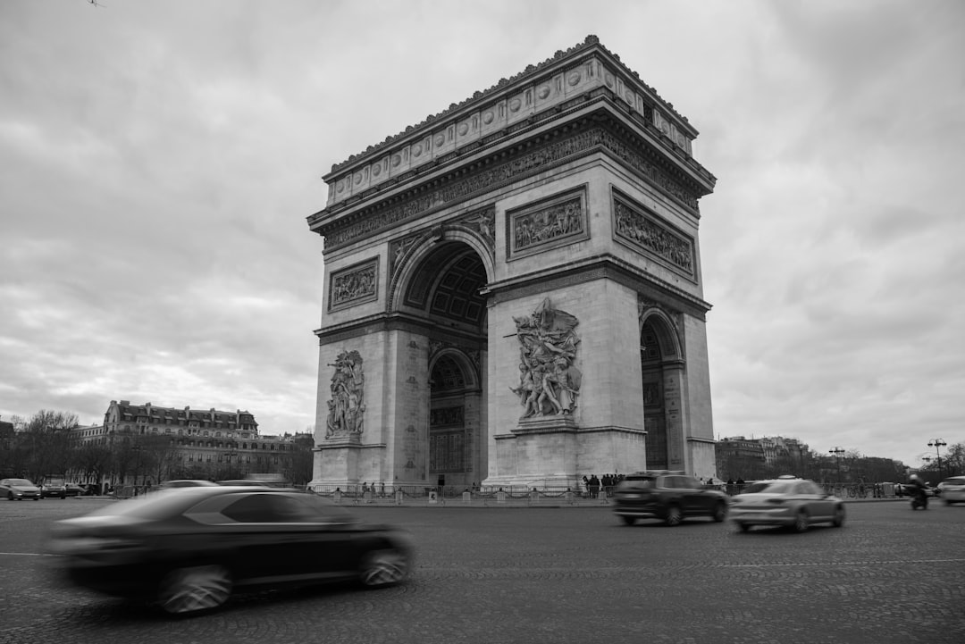 a black and white photo of cars passing by the arc of triumph, Arc de Triomphe - monumental