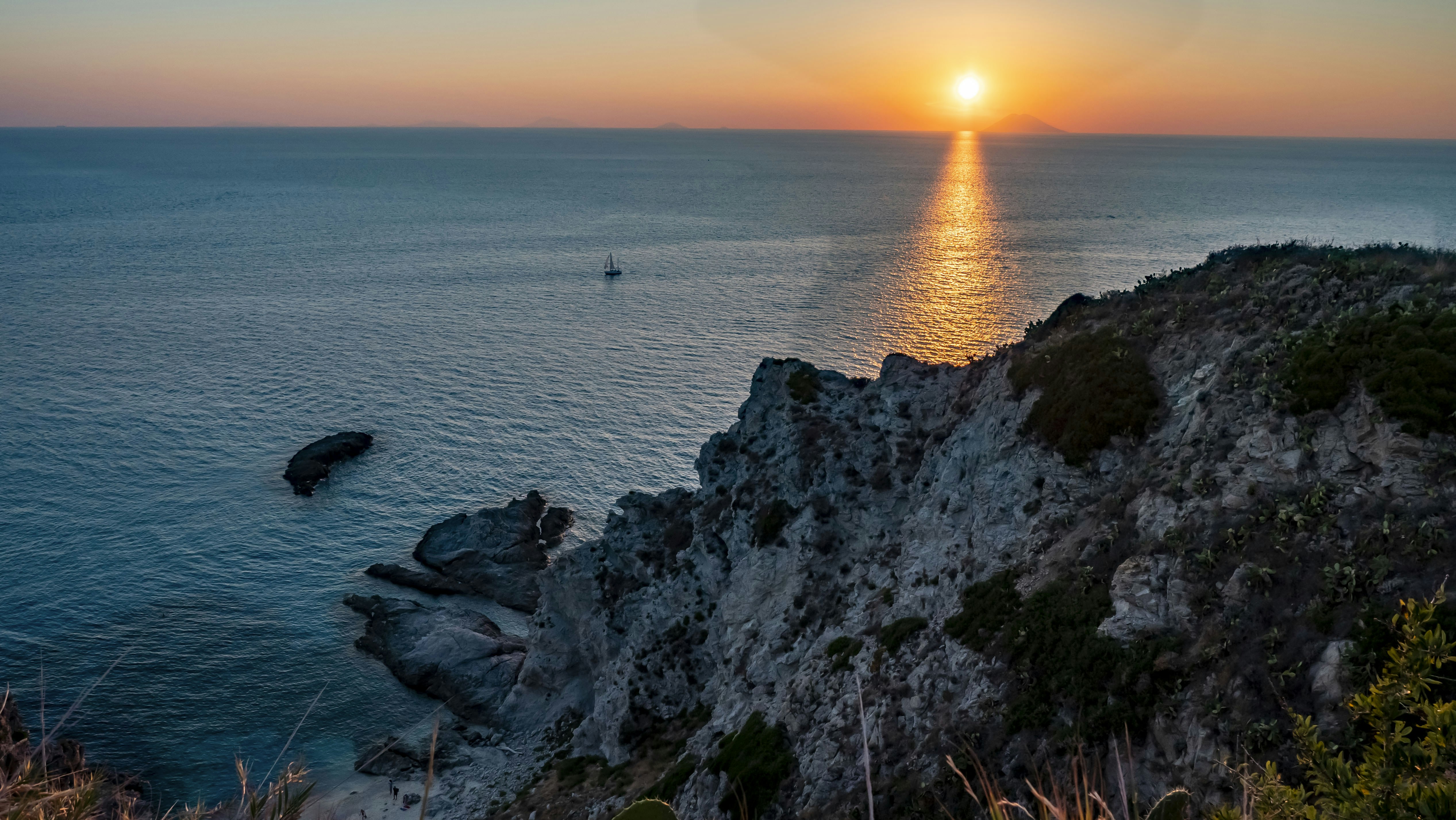 the sun is setting over the ocean with a boat in the distance