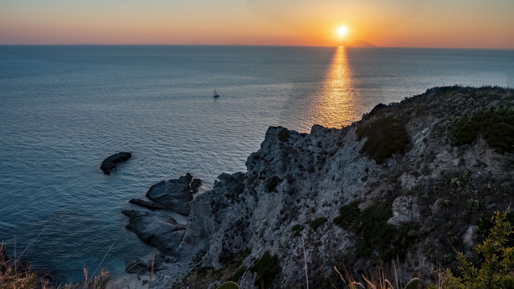 the sun is setting over the ocean with a boat in the distance