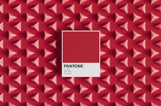 A pattern of three-dimensional red and pink pyramids on a red background with a central focus on a Pantone color swatch labeled 'True Red', including the color code 19-1664 and hex code #BF1932.