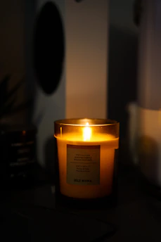 Close-up of a luxury scented candle softly glowing in a dark, elegant room with golden accents