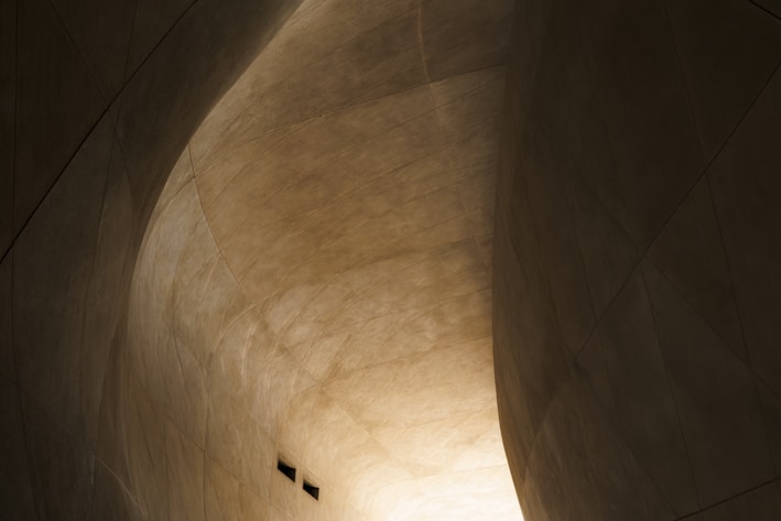 A sculptural detail showing the interplay of light and shadow on a smooth, curved form with restrained yellow highlights adding warmth.