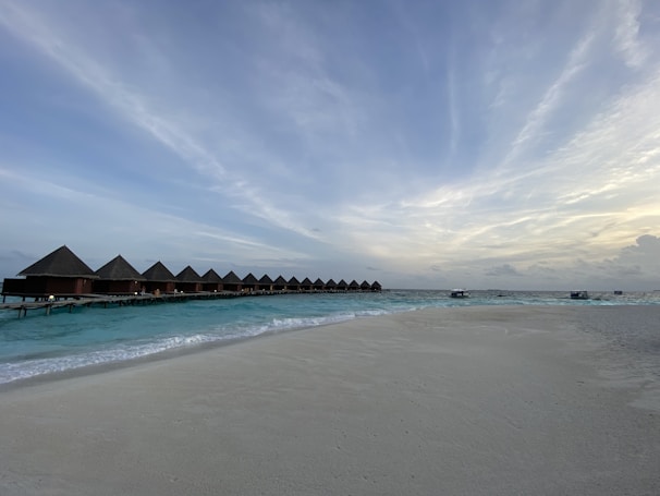 A serene beach scene in the Maldives with crystal-clear turquoise water and overwater bungalows glowing under a golden sunset.