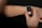 A person interacts with a smartwatch on their wrist, using a finger to select an app on the watch's touchscreen. The smartwatch has a white strap and a black, illuminated display showcasing multiple colorful app icons. The background is dark, highlighting the focus on the device and hand.