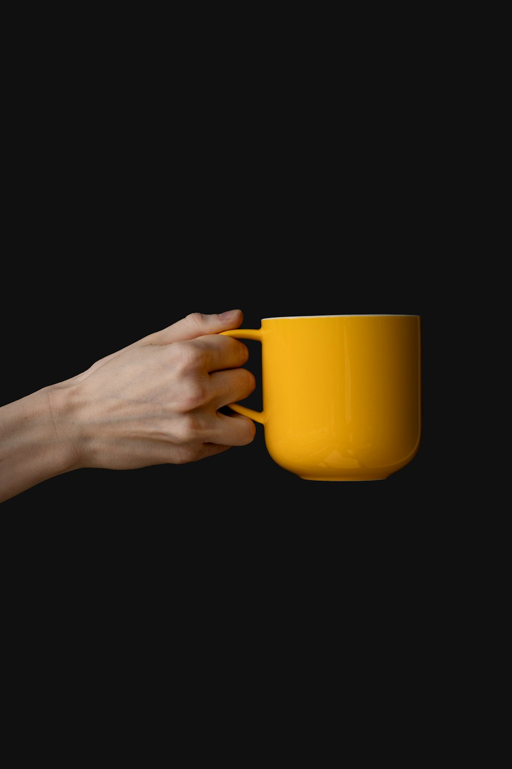 a person's hand holding a yellow coffee cup