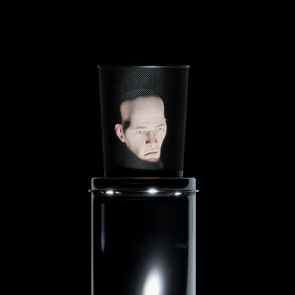 a man's face is reflected in a black container