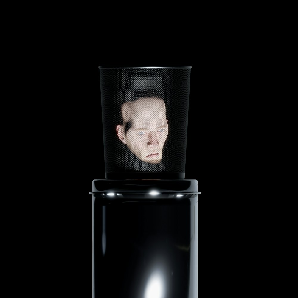 Il volto di un uomo si riflette in un contenitore nero