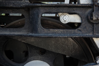 A close-up view of the metal components of a machine, showcasing a dark, weathered steel structure with circular openings and visible bolts. The metal surface appears worn and slightly rusty, indicating age or heavy use.