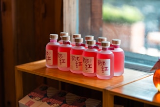 Bottles of foleré de macé lined up with deep red hibiscus and green leaves in the background.