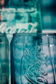 A close-up view of a clear glass bottle with embossed lettering and a textured surface, reflecting a bluish hue from the background lighting.