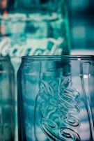 A close-up view of a clear glass bottle with embossed lettering and a textured surface, reflecting a bluish hue from the background lighting.