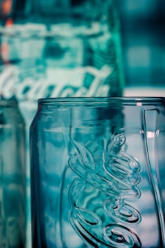 A close-up view of a clear glass bottle with embossed lettering and a textured surface, reflecting a bluish hue from the background lighting.