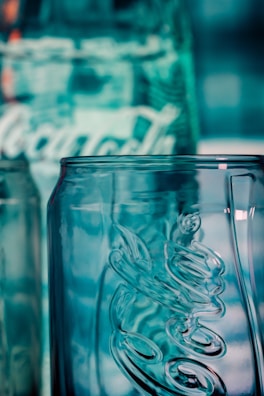 A close-up view of a clear glass bottle with embossed lettering and a textured surface, reflecting a bluish hue from the background lighting.