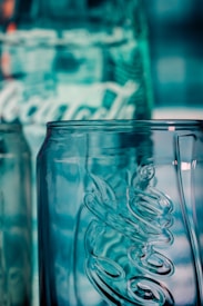 A close-up view of a clear glass bottle with embossed lettering and a textured surface, reflecting a bluish hue from the background lighting.