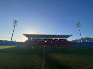 Wide shot of an empty stadium at twilight, emphasizing sharp shadows and deep contrasts.