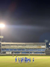 Team huddle on the field under bright stadium lights, players wearing sky blue and electric blue jerseys.