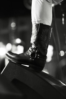 Close-up of a pair of tall leather boots with intricate stitching, set against a neutral background.