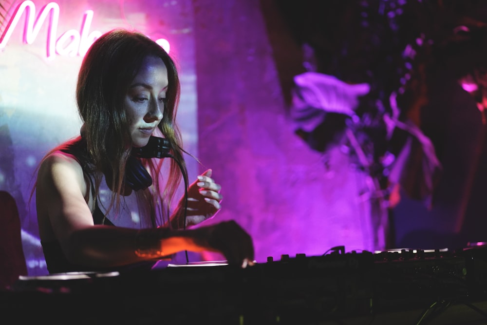 a woman sitting at a keyboard in front of a neon sign