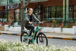A happy tourist riding an e-bike along a tree-lined path inside Central Park with skyscrapers in the background