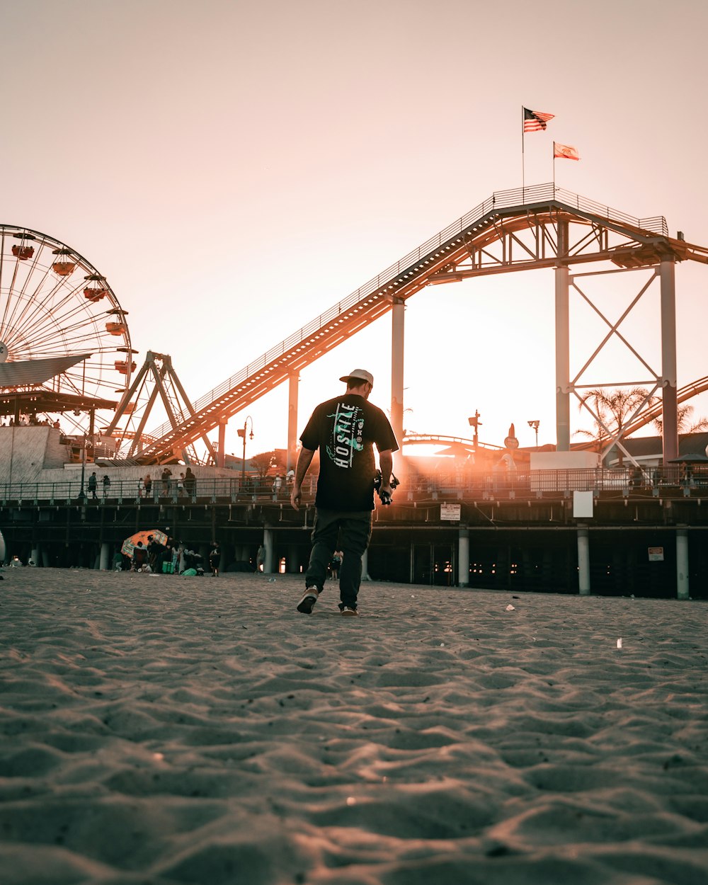 a man walking on a sandy beach next to a ferris wheel