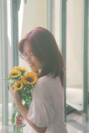 A happy customer holding a la belle petalova floral bouquet with a warm smile in a sunlit room.