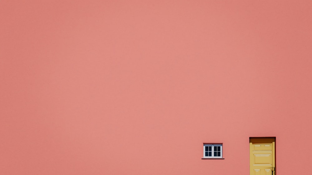 a pink wall with a yellow door and window