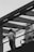 A person standing on a modern glass railing walkway, seemingly lost in thought while smoking. The scene is captured in black and white, giving it a nostalgic and contemplative feel. Overhead, there is a clear sky and the background features part of a tall urban building.