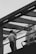 A person standing on a modern glass railing walkway, seemingly lost in thought while smoking. The scene is captured in black and white, giving it a nostalgic and contemplative feel. Overhead, there is a clear sky and the background features part of a tall urban building.