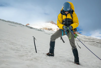 a man in a yellow jacket climbing up a snowy mountain