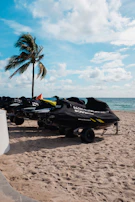A group of friends laughing and gearing up beside sleek jet skis on the sandy shore.