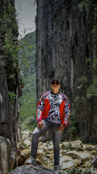 A close-up of a rugged jacket made from colorful secondhand fabric, set against a backdrop of rocky mountain cliffs.