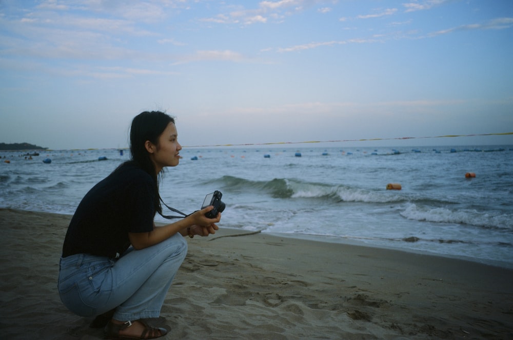 a woman kneeling on a beach holding a camera