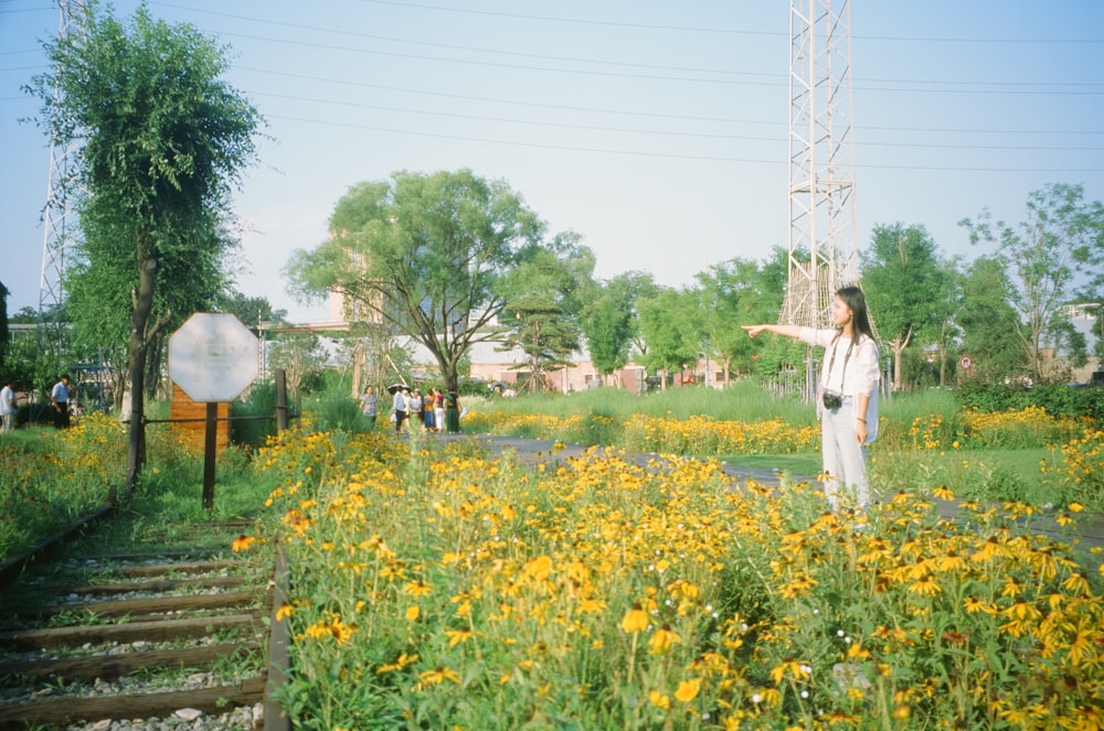 a woman pointing at something while standing in a field of flowers
