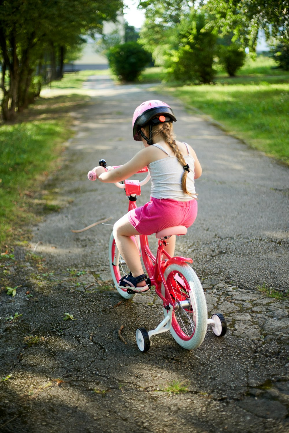 a little girl riding a pink bike down a dirt road