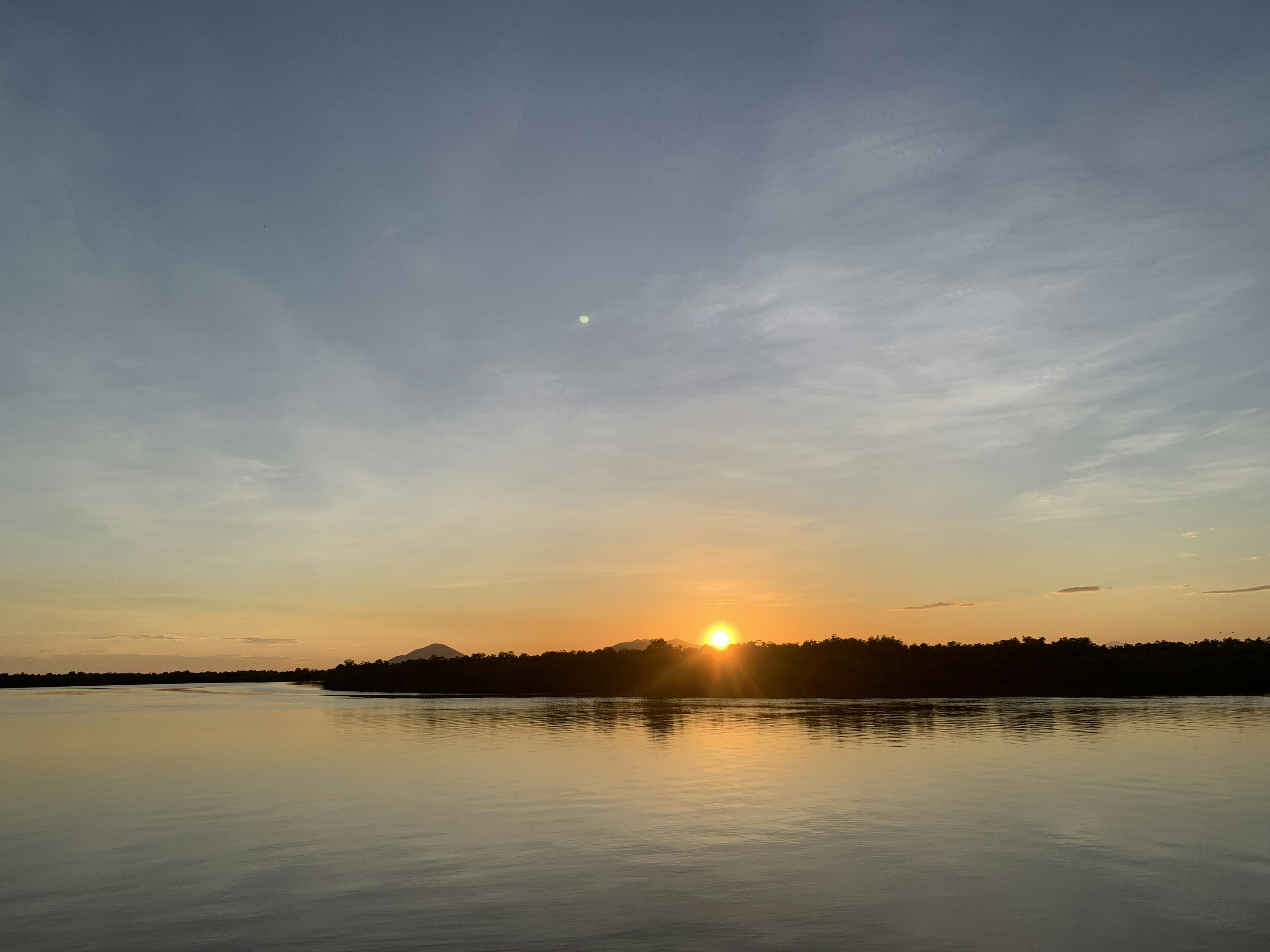 Coucher de soleil sur un fleuve avec reflets orangés dans l'eau calme