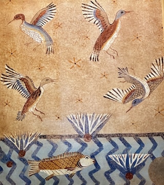 A mural illustrating birds in flight and fish swimming in a stylized aquatic scene. The background features a textured beige surface with small star-like patterns. The birds have vividly colored wings with shades of blue, brown, and white, while the fish are depicted below in a blue, zigzagged water pattern. There are also abstract geometric plant-like shapes present.