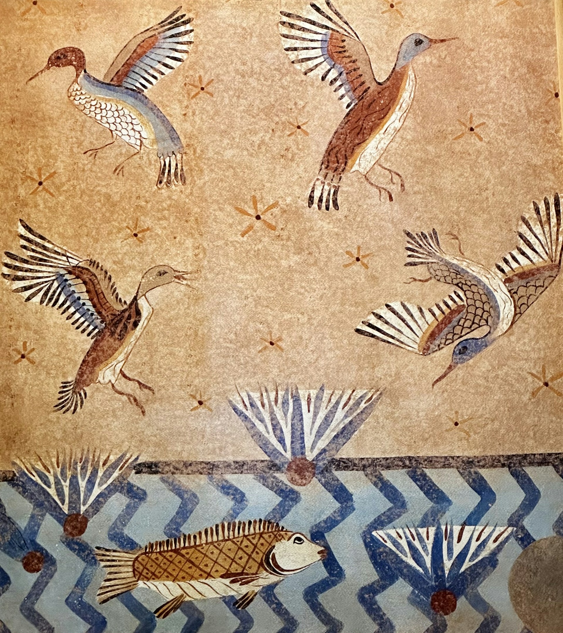 A mural illustrating birds in flight and fish swimming in a stylized aquatic scene. The background features a textured beige surface with small star-like patterns. The birds have vividly colored wings with shades of blue, brown, and white, while the fish are depicted below in a blue, zigzagged water pattern. There are also abstract geometric plant-like shapes present.