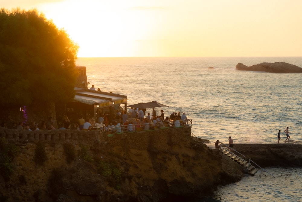 a group of people standing on top of a cliff next to the ocean