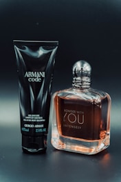 A black tube labeled 'Armani Code' and a clear bottle with amber liquid labeled 'Stronger With You Intensely' are positioned side by side on a dark background.