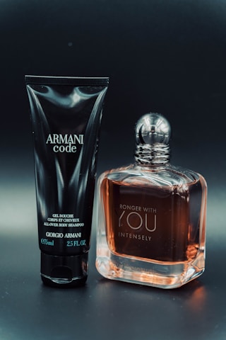 A black tube labeled 'Armani Code' and a clear bottle with amber liquid labeled 'Stronger With You Intensely' are positioned side by side on a dark background.