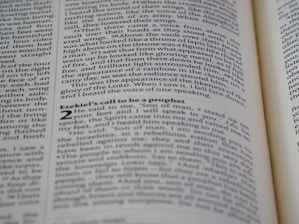 A close-up shot of an open book displaying text on both visible pages, with focus on the text about Ezekiel's call to be a prophet. The text is printed in two columns, and the alignment of the words is neat and justified.