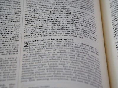 A close-up shot of an open book displaying text on both visible pages, with focus on the text about Ezekiel's call to be a prophet. The text is printed in two columns, and the alignment of the words is neat and justified.