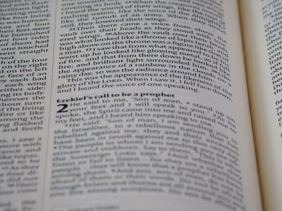 A close-up shot of an open book displaying text on both visible pages, with focus on the text about Ezekiel's call to be a prophet. The text is printed in two columns, and the alignment of the words is neat and justified.