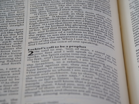 A close-up shot of an open book displaying text on both visible pages, with focus on the text about Ezekiel's call to be a prophet. The text is printed in two columns, and the alignment of the words is neat and justified.