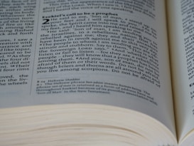 A close-up view of an open book displaying a passage from the Bible, specifically Ezekiel's call to be a prophet. The text is in English and features numbered verses.