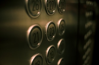 A close-up view of elevator buttons with numbers in a vertical arrangement. The buttons are metallic and slightly reflective, with a soft focus on the background.