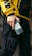 A person wearing a yellow jacket with bold black letters and black cargo pants is holding a smartphone. The jacket has a sporty, urban style, and the phone is held in a casual grip.