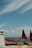 A scenic view with rooftops of orange tiles and historic buildings overlooking a large body of water under a sky with scattered clouds. In the foreground, there are small model trams adorned with Portuguese flags.